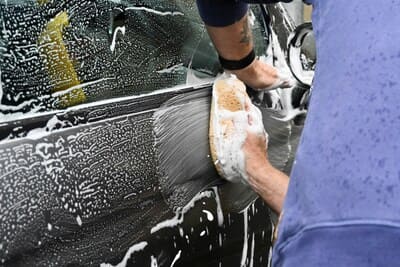 Un homme lave une voiture avec une éponge, concentré sur sa tâche. 