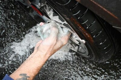 Une personne lave le pneu d'une voiture avec une éponge et de l'eau. 